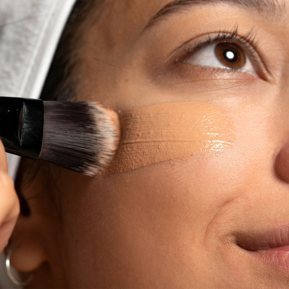 women is using brush swipes foundation on face