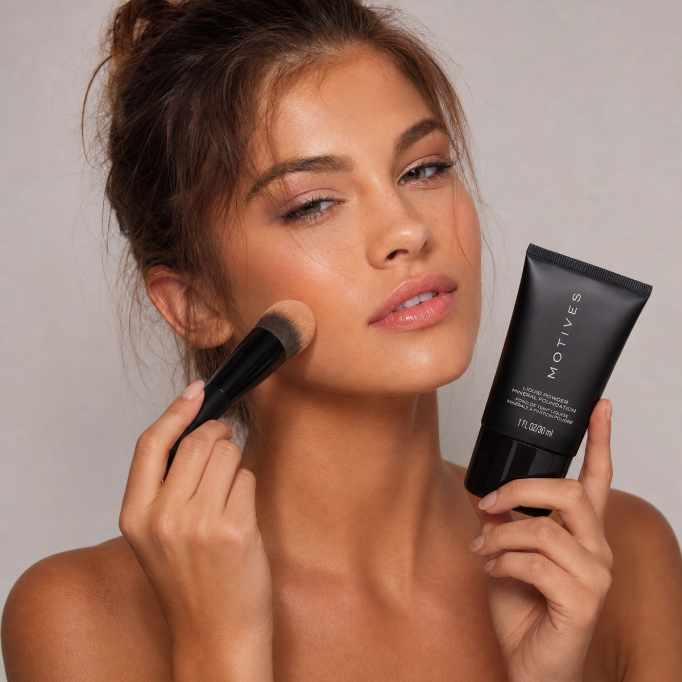 woman with a brush to her face and Motives Liquid Powder in her hand